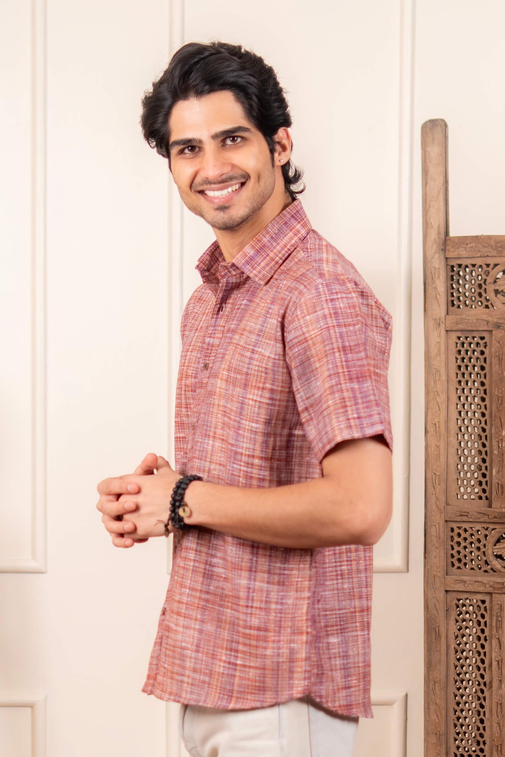Man wearing a red checkered shirt standing against a white wall with wooden decor.