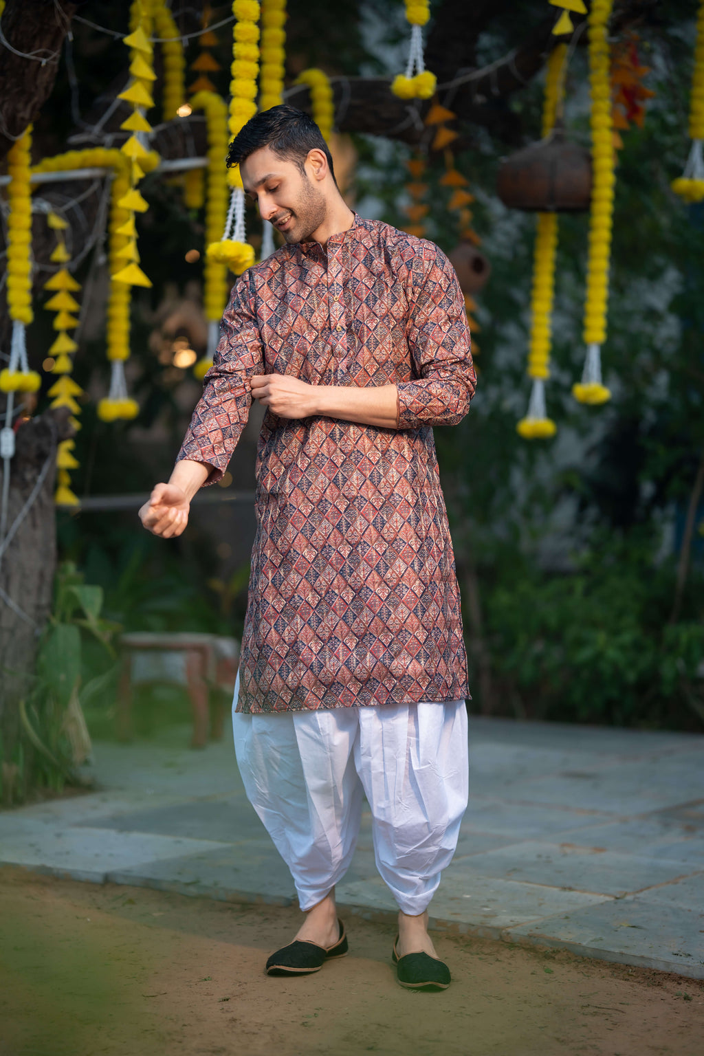 indian man wearing a multicolor kurta with dhoti. standing in front of a wedding decor. 