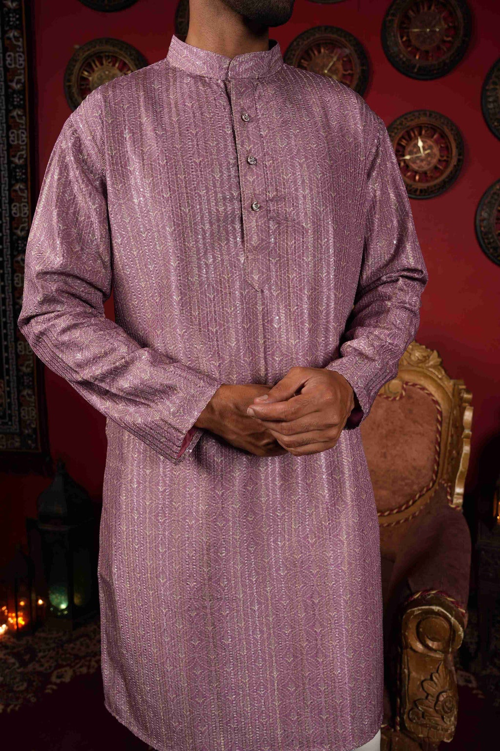 Man in a pink kurta standing in a room with decorative wall art and furniture.