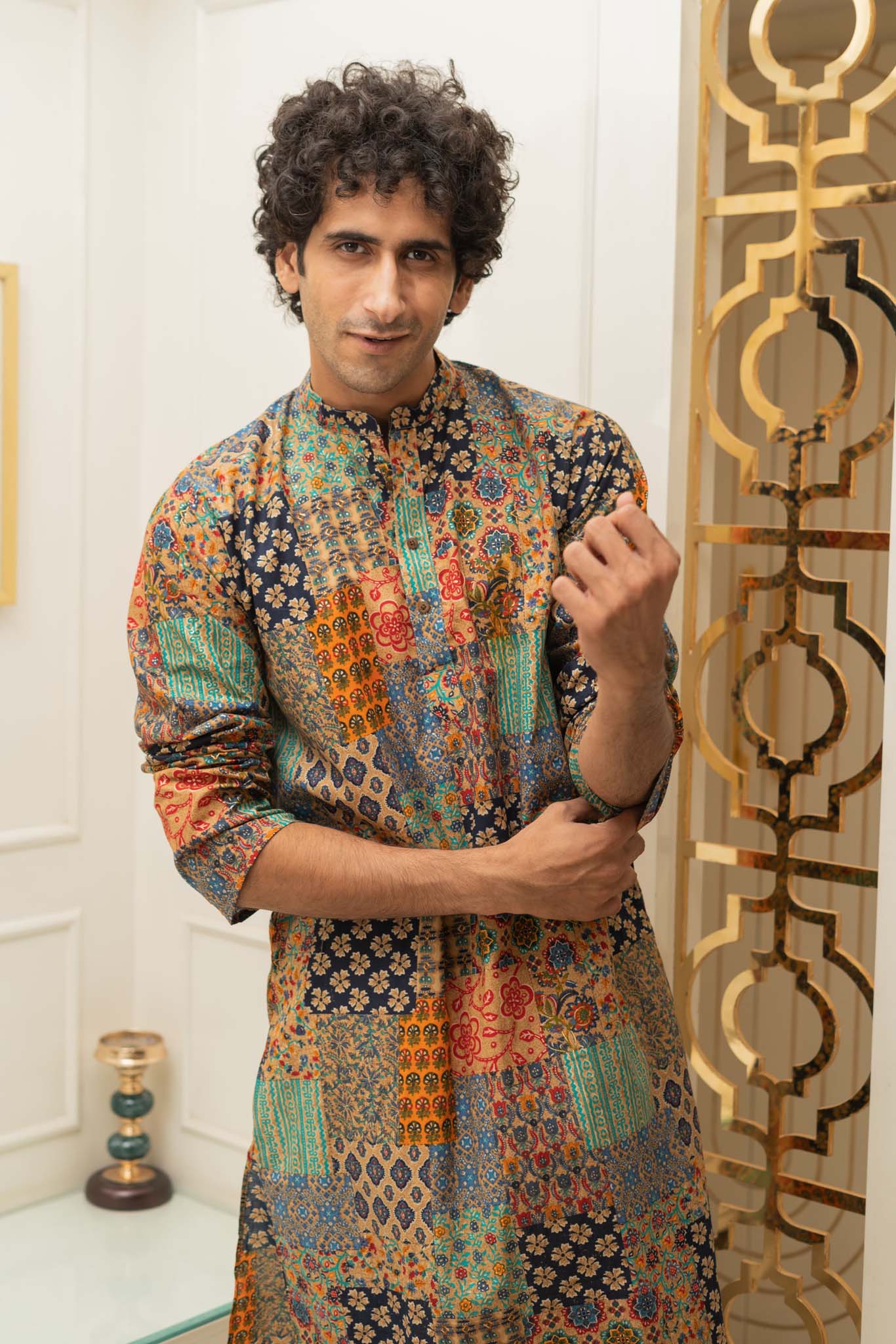 Man wearing a colorful patterned kurta standing in a room with decorative elements.