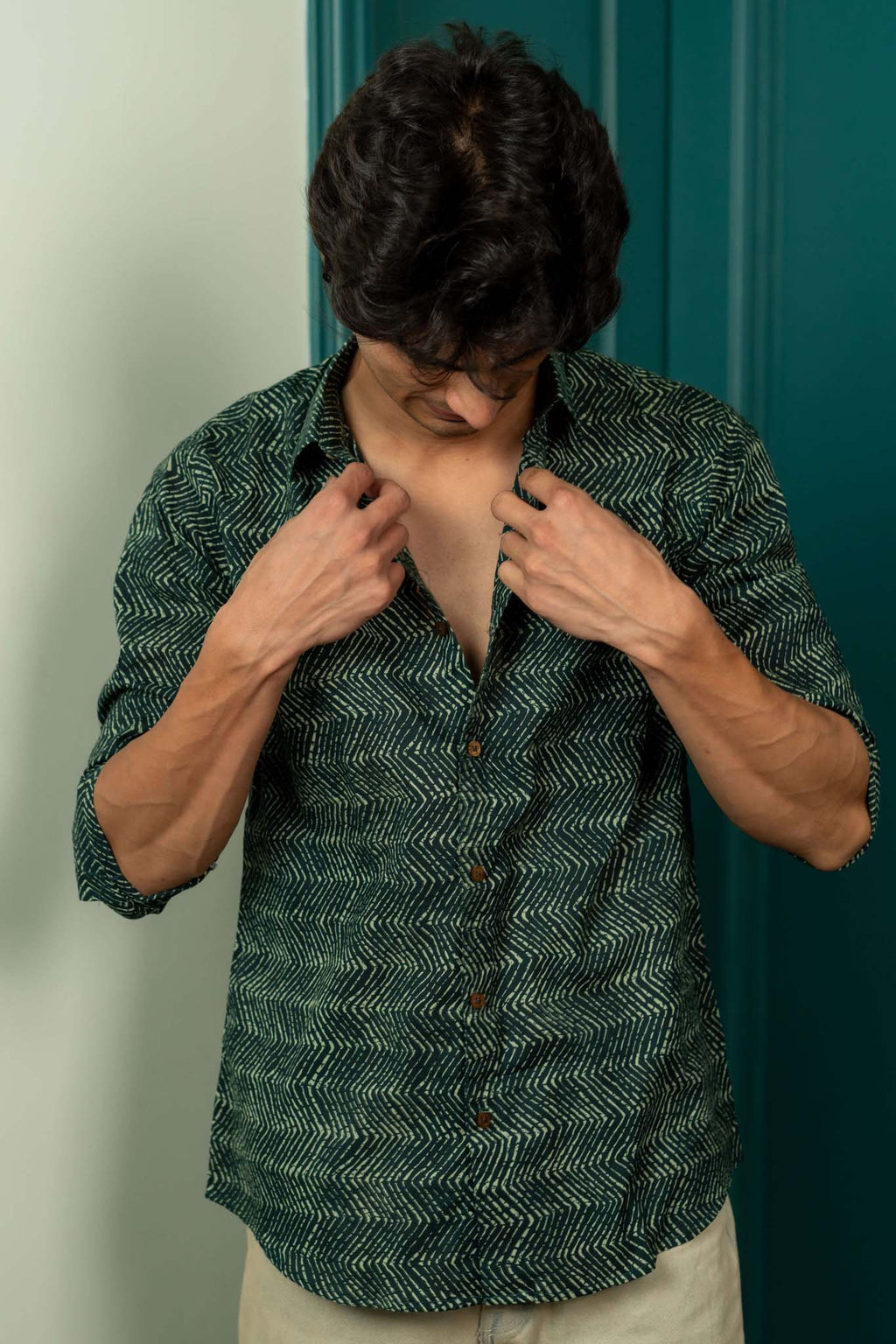 Person wearing a green patterned shirt against a green door.