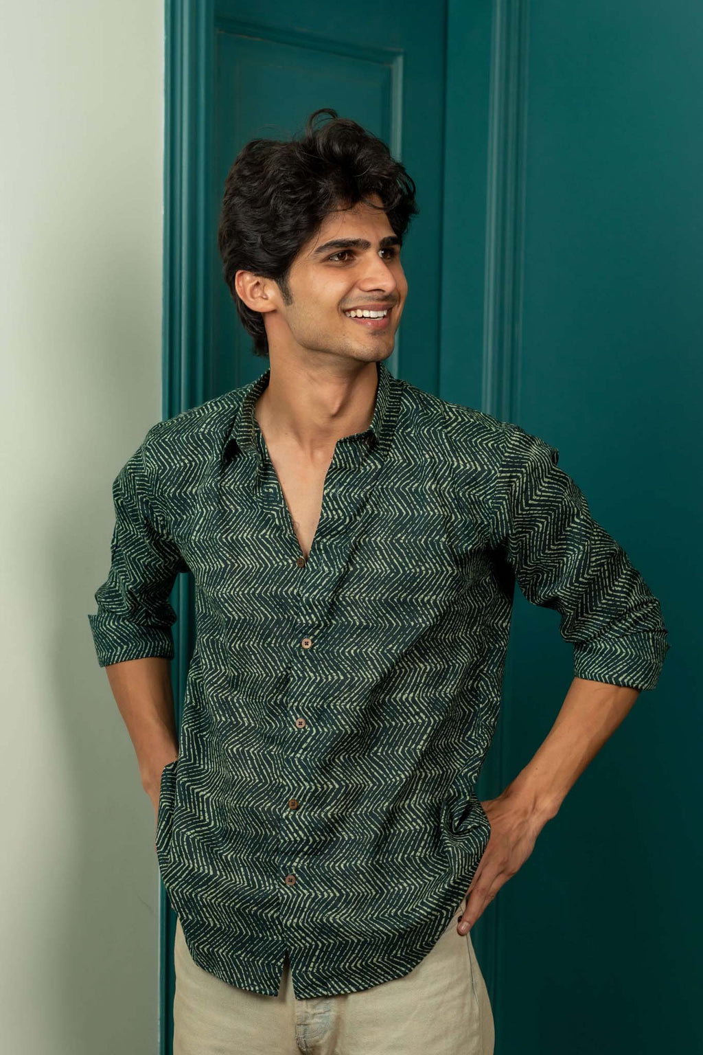 Man wearing a green patterned shirt standing against a teal door.