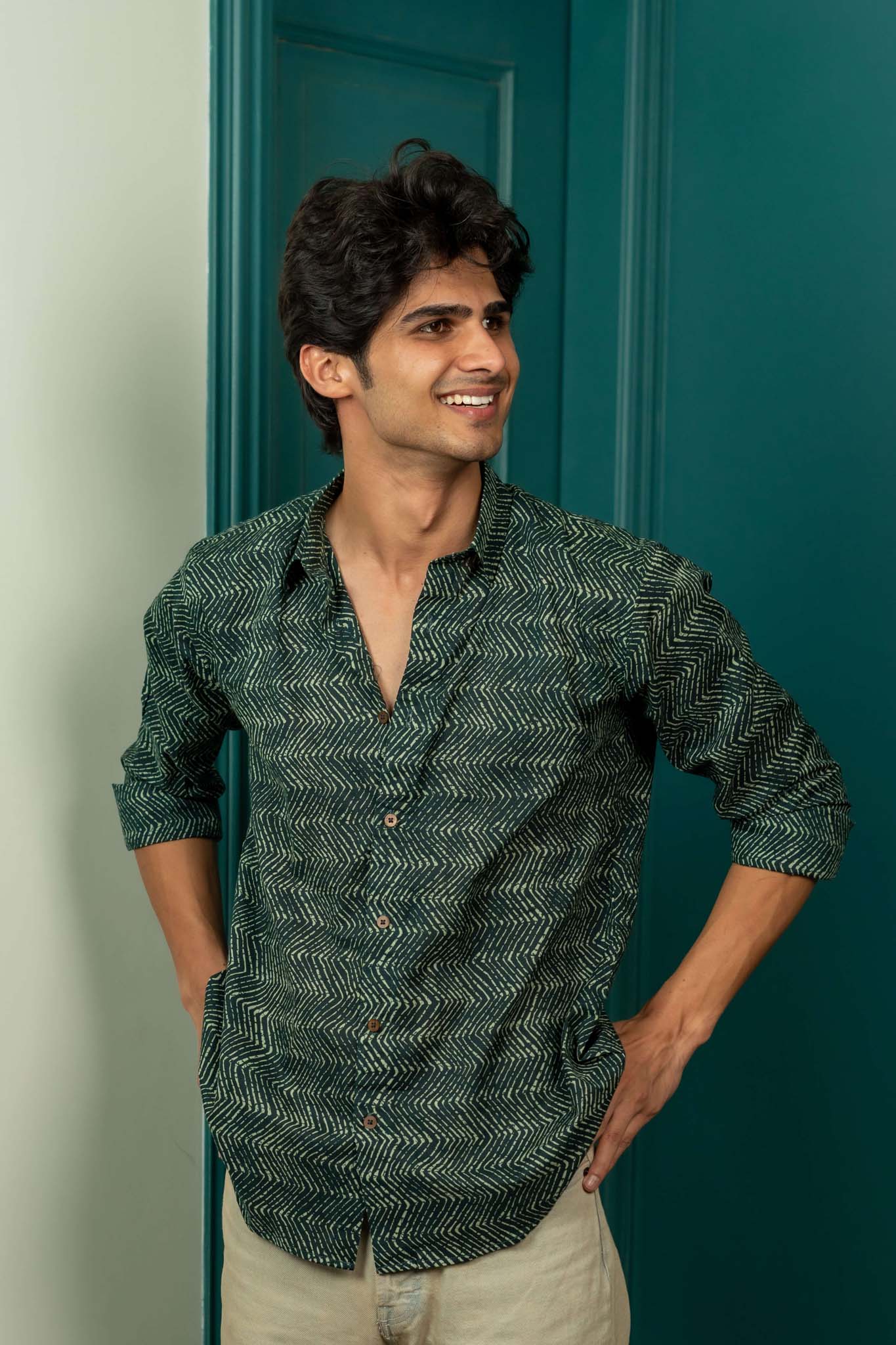 Man wearing a green patterned shirt standing against a teal door.