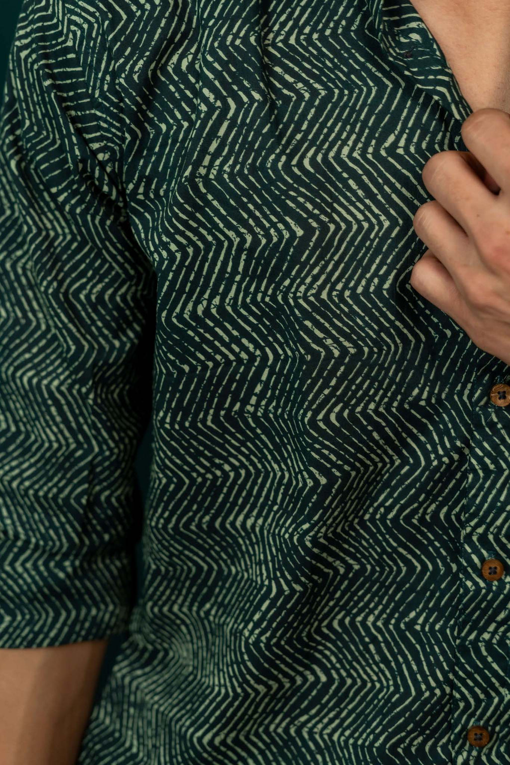 Close-up of a green patterned shirt with a hand adjusting it.